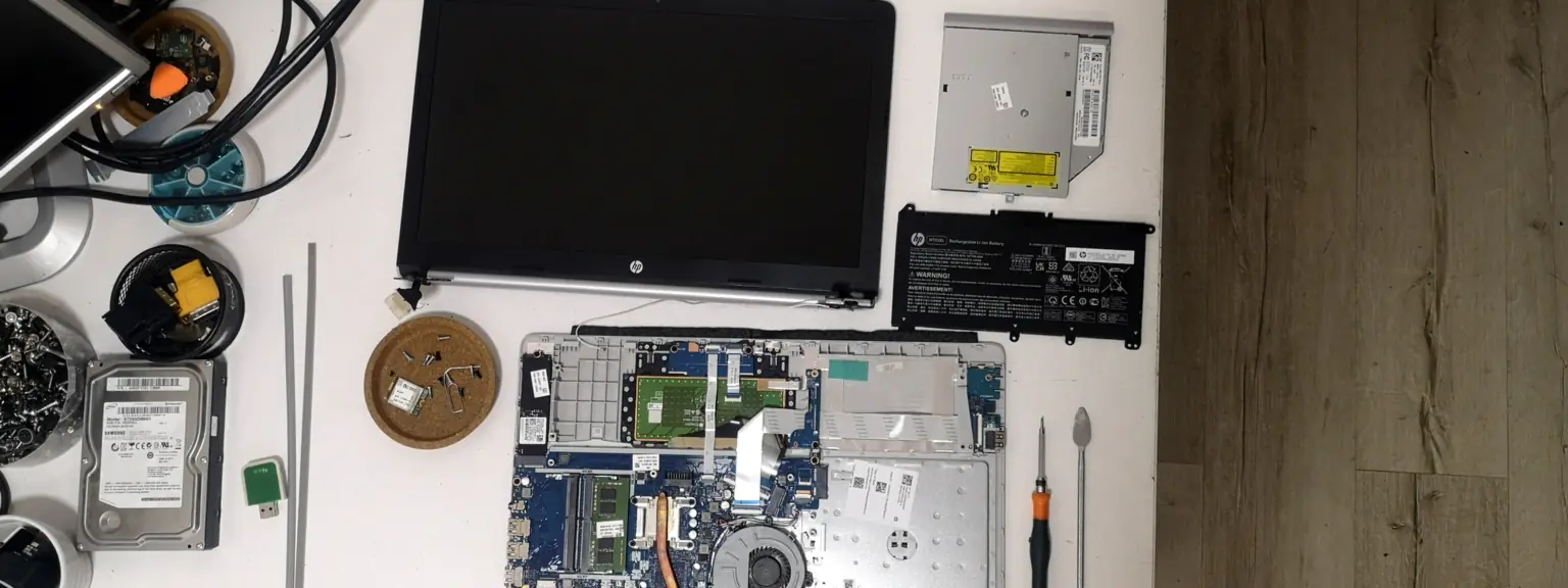 Αποσυναρμολογημένο laptop σε πάγκο επισκευής, με την οθόνη δίπλα