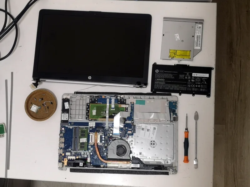Laptop αποσυναρμολογημένο σε πάγκο επισκευής, με την οθόνη και τη μπαταρία δίπλα